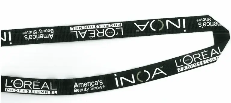 Black custom baseball trading pin lanyard with white LOréal Professionnel, INOA, and Americas Beauty Show logos repeating.