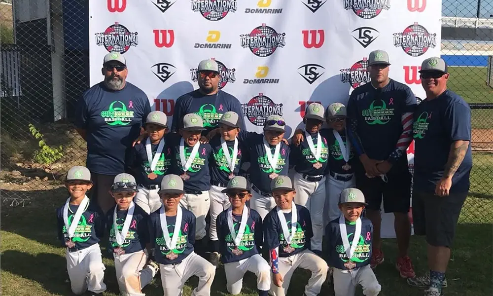 Youth baseball team with custom trading pins, uniforms, and medals after USSSA World Series 2025 group photo on field.