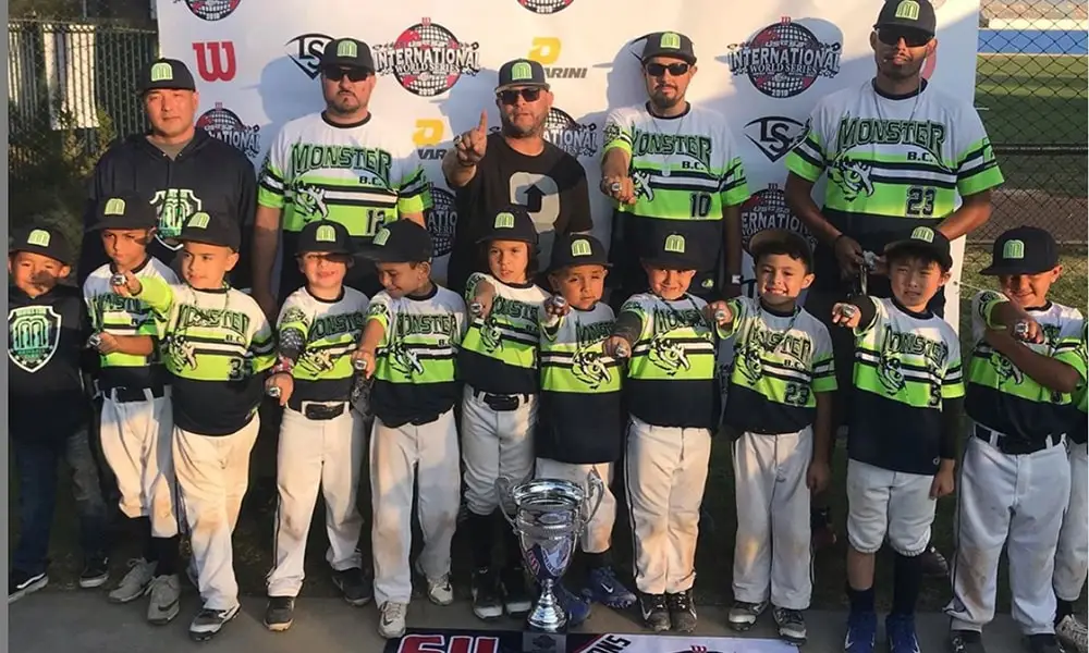 Youth baseball team in green uniforms celebrates USSSA World Series win with trading pins, trophy, banner, medals, and coaches.